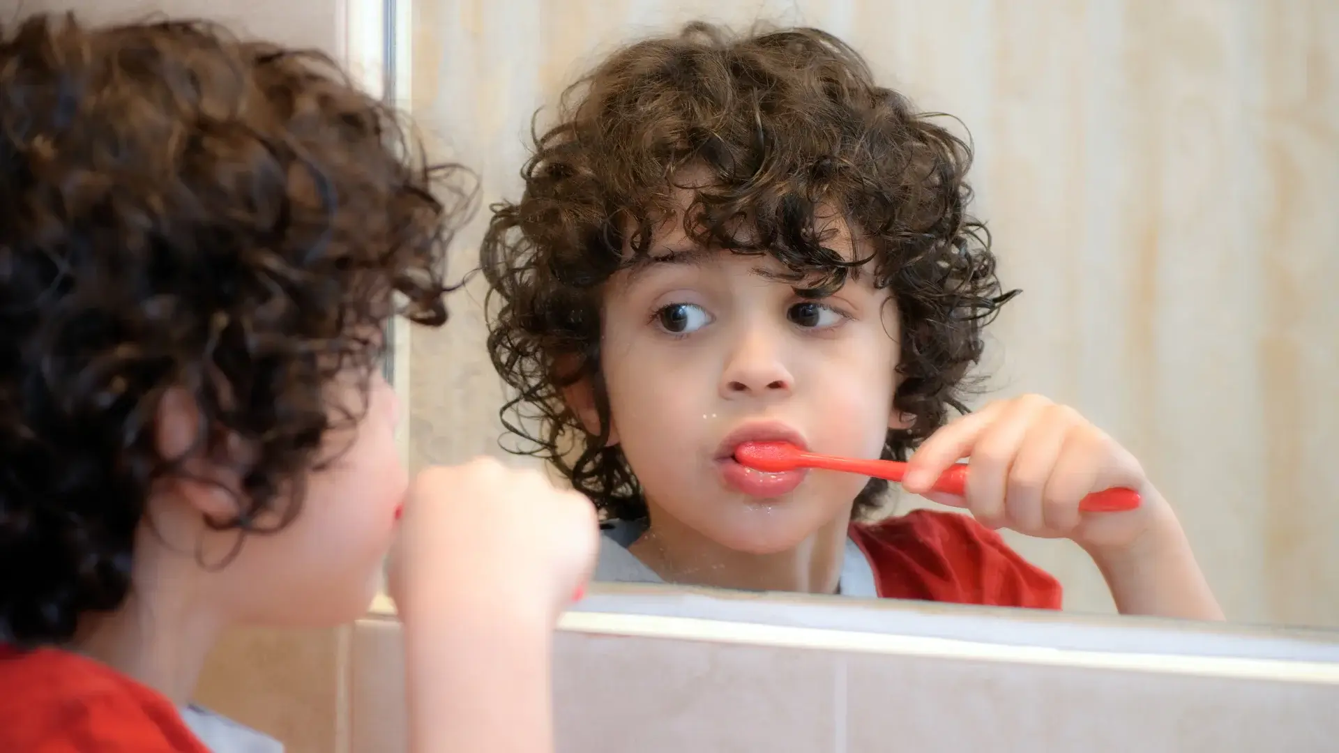 A child brushing his teeth and looking in the mirror
