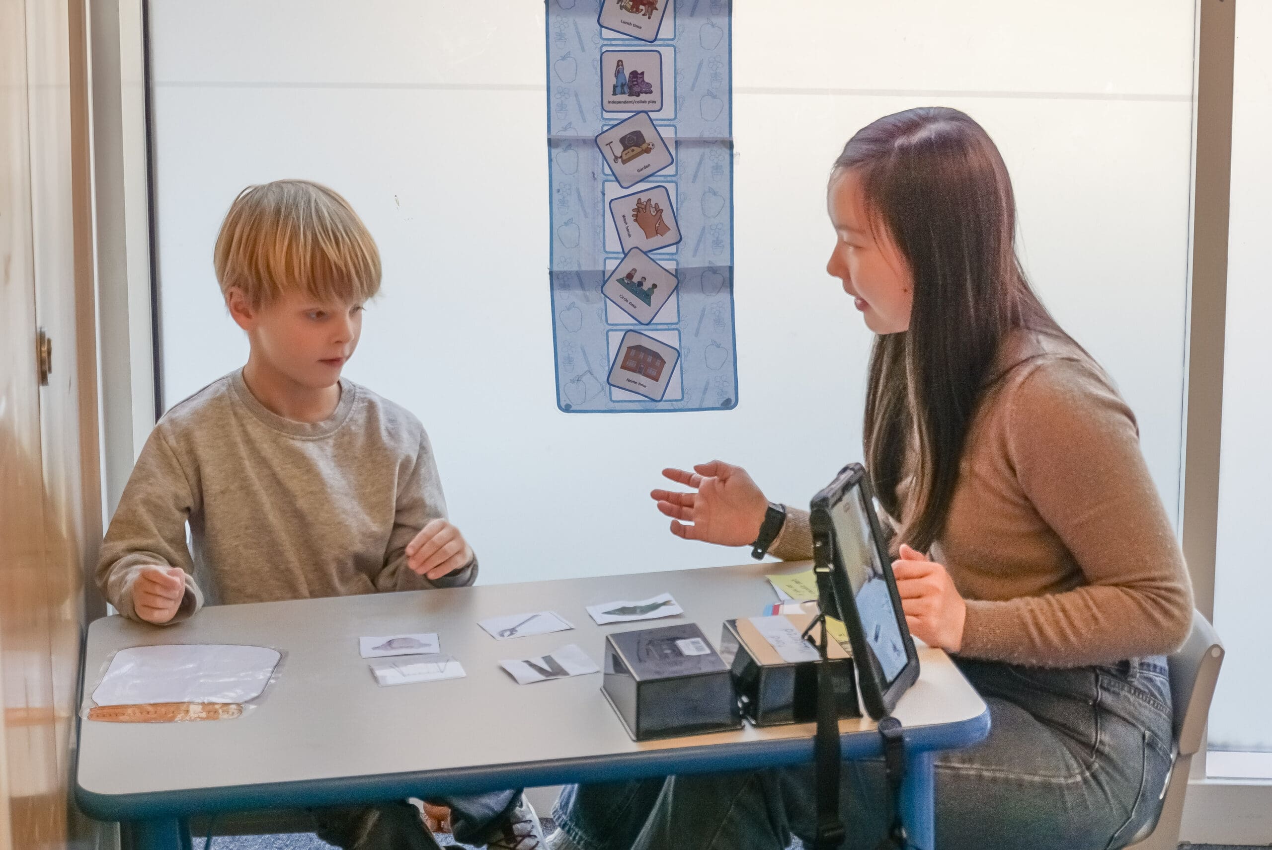 A young Autistic child smiles while playing in a vibrant, sensory-rich environment, guided by a supportive ABA therapist. The scene highlights First Bridge Centre's nurturing and structured approach to early intervention that is perfectly aligned with the enriching experiences offered during our summer school programme.